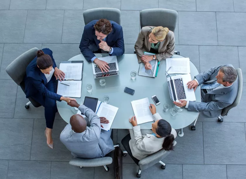 A top-down view of people sitting around an oval meeting table